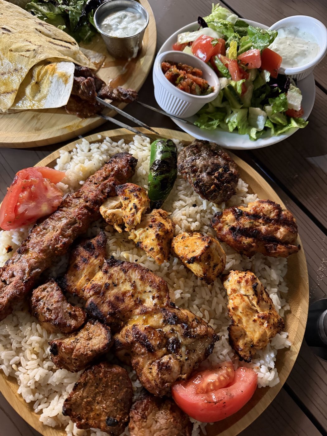 A platter of grilled chicken, lamb and beef kebabs over rice with salad and ezme.