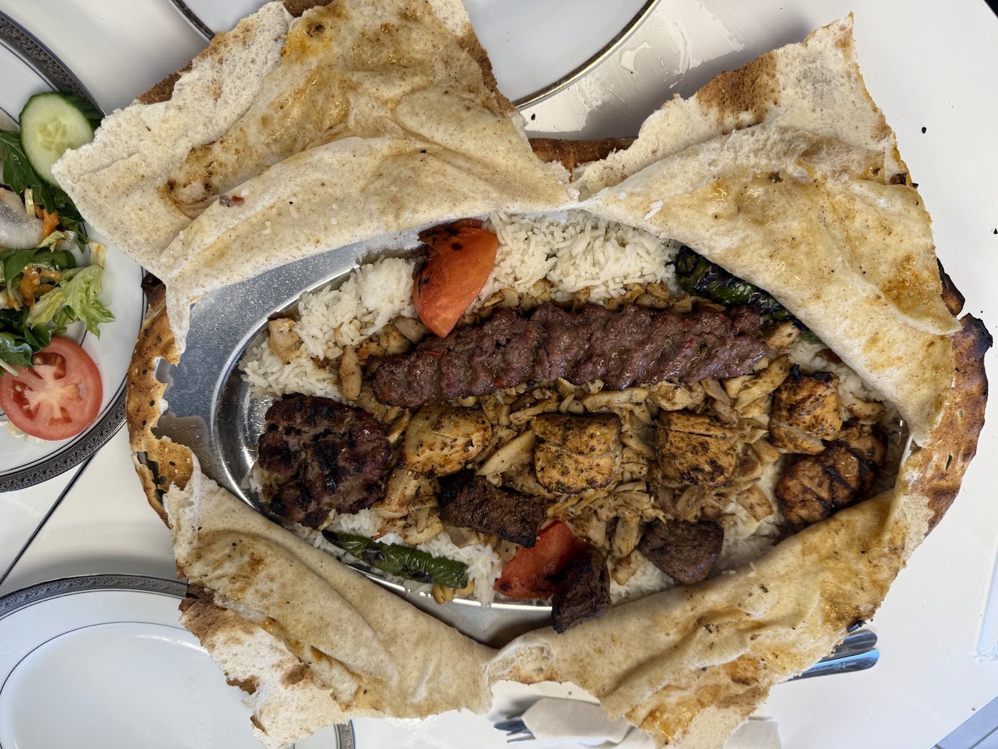 A mixed grill of lamb, chicken and kofta over rice, framed by puffed Turkish bread.